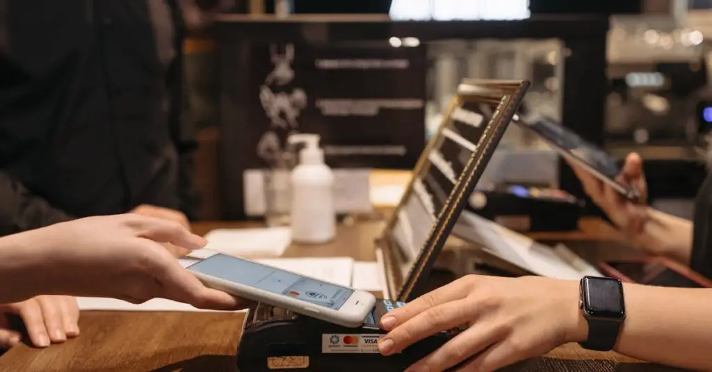 Hands using mobile for contactless payment at café terminal.